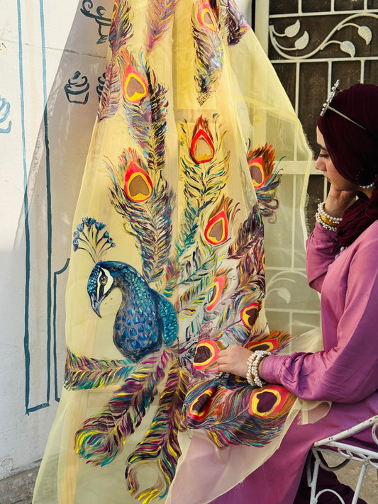 Model holding Moor hand painted organza dupatta featuring a blue peacock and colorful feather design
